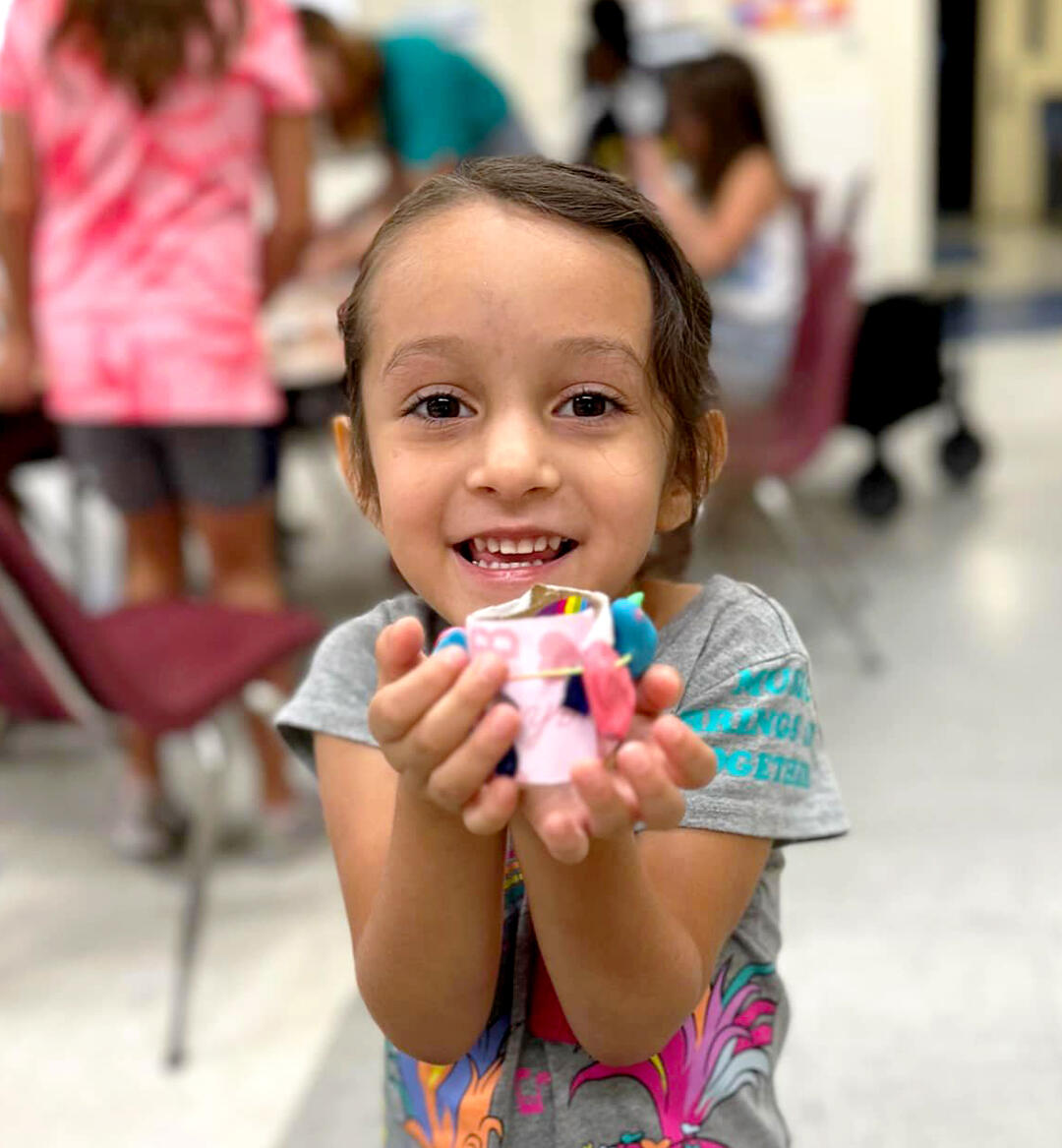 Young girl holding up arts and crafts while smiling