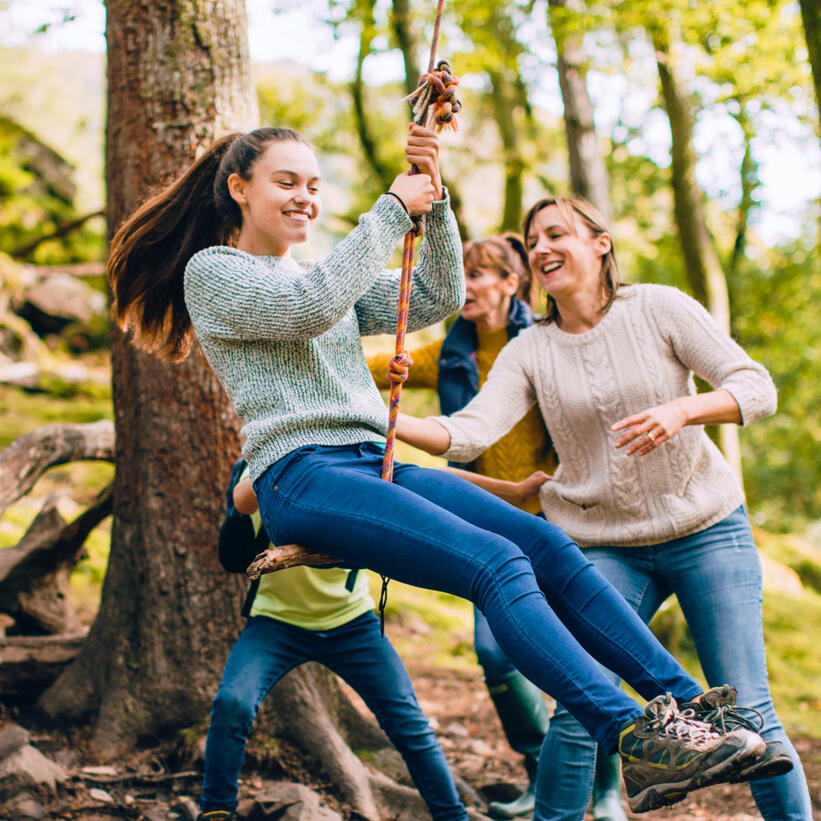 Teenager and younger child taking turns on tree swing with guardians